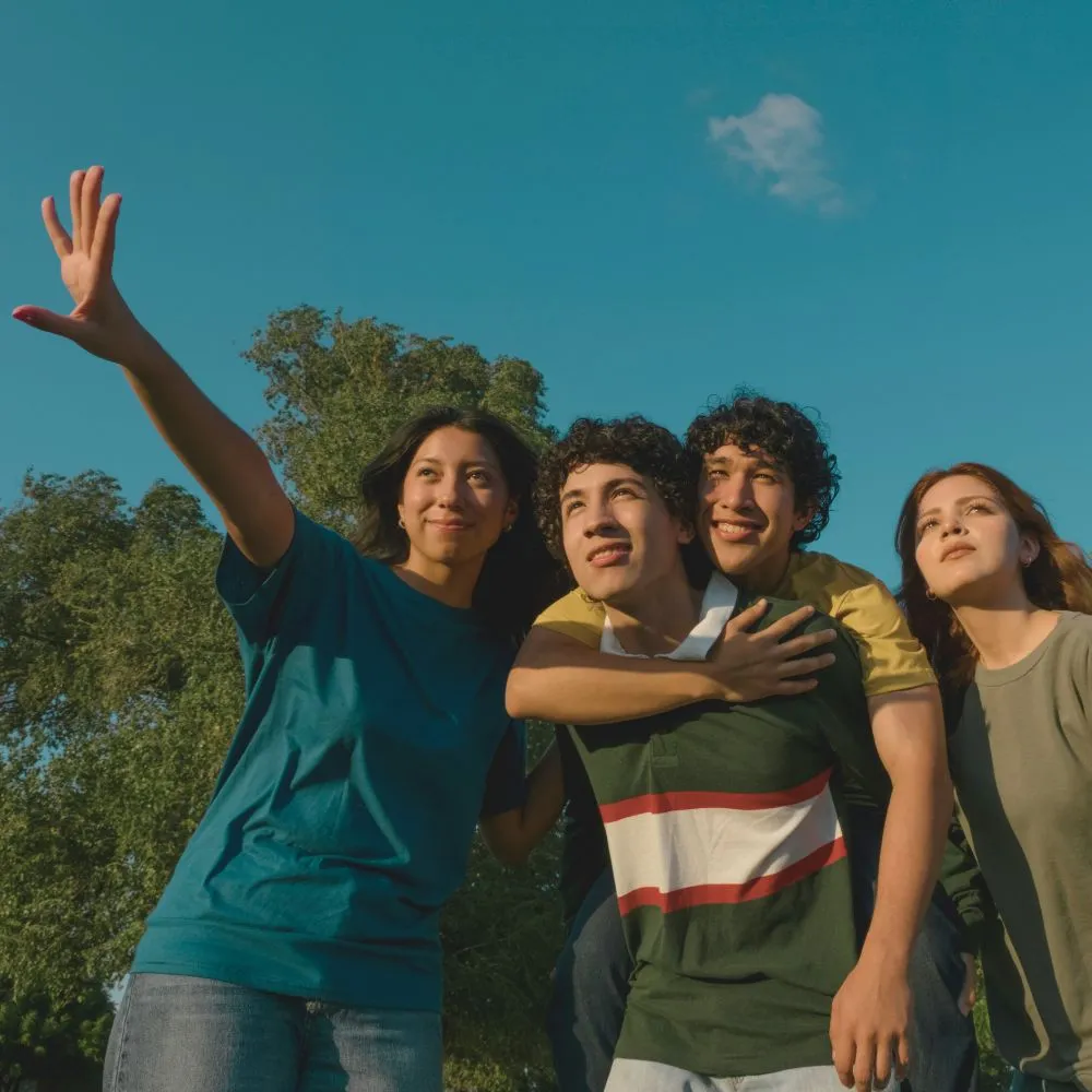 A group of young people outdoors, smiling and reaching out together, symbolizing unity and positive social impact, reflecting the company’s commitment to community well-being.